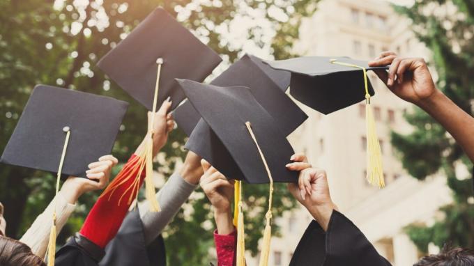 Група многонационални студенти празнуват дипломирането си, като хвърлят шапки във въздушния план. Концепция за образование, квалификация и рокля.
