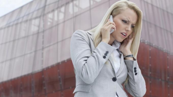 Жена с ADHD слуша някого на мобилен телефон и се ядосва пред висока сграда