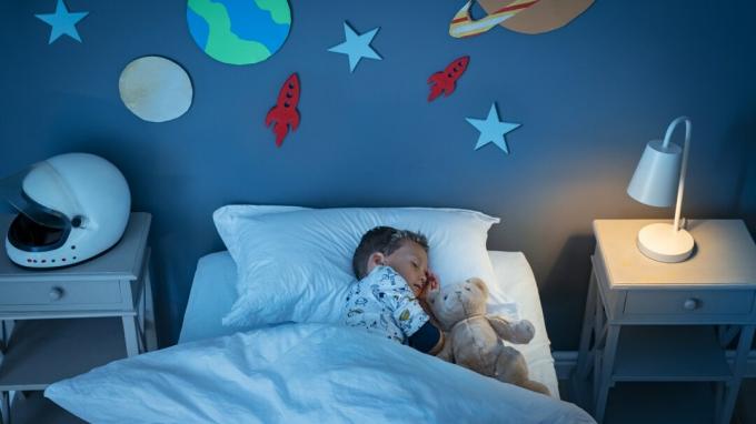 Гледка под висок ъгъл на малко момче adhd, което мечтае да стане астронавт, докато спи с плюшено мече в стая, декорирана в космоса.